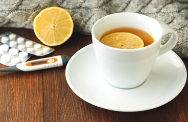  mug with hot tea, thermometer and pills  on wooden surface, flu season in autumn