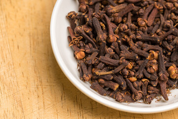 Cloves in a white bowl on wooden table