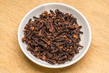 Cloves in a white bowl on wooden table