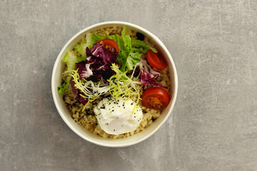 Healthy bowl with poached egg, bulgur, tomatoes and lettuce on a gray background in an eco paper box. Healthy food delivery concept.