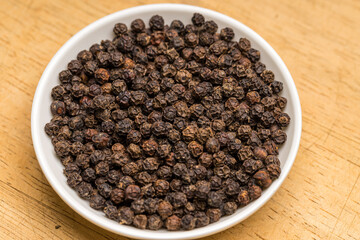 Black pepper in a white bowl on wooden table
