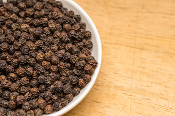 Black pepper in a white bowl on wooden table