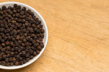 Black pepper in a white bowl on wooden table