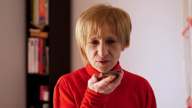 Blonde woman recording message using voice on smartphone. Happy woman recording audio on mobile phone ah home.