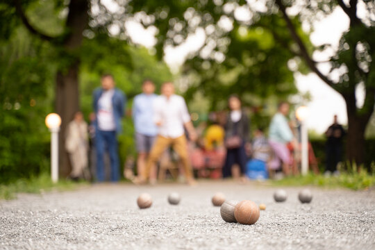 Friends Playing Bocce Game Guy Through A Ball Above Green Trees Park In City Park In Summer Sunset Light	