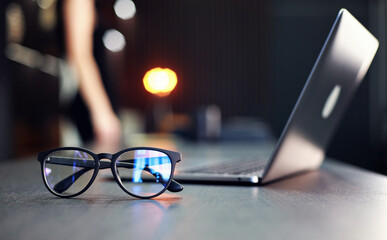 Glasses and laptop on table with woman silhouette in black.