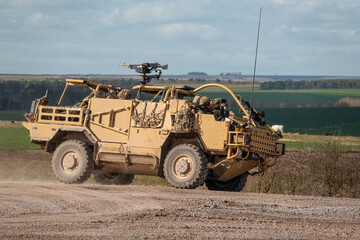 British army Supacat Jackal 4x4 rapid assault, fire support and reconnaissance vehicle in action across open countryside on a military battle training exercise