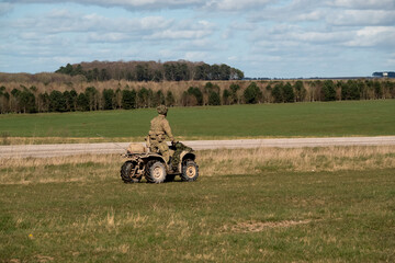 Obraz premium British army soldier driving a small ATV quad bike across open countryside on a military exercise