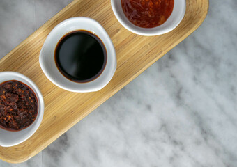 Top view of 3 Asian sauces on a bamboo tray on a light marble surface.