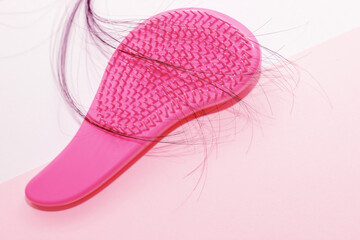 Comb plastic pink and fallen hair on a cardboard background.