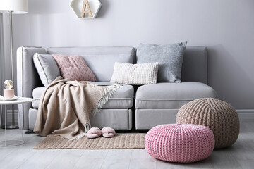 Stylish knitted poufs near sofa in living room. Interior element