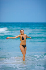 A young girl in a green bathing suit stands by the sea and laughs with her arms outstretched. High quality photo