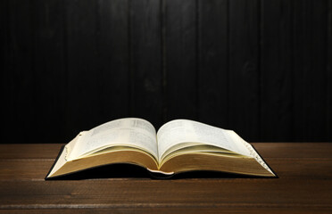 Open Bible on table against black wooden background. Christian religious book