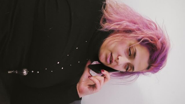 Young woman with pink hair speaking on the phone. She is sitting on the sofa at home. vertical video