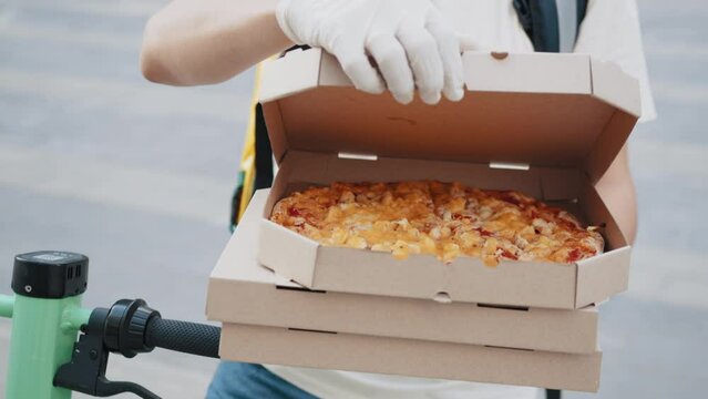 Pizza Delivery. Close up Unrecognizable Delivery Man Wearing Medical Mask and Gloves with Pizza Box Close Up. Delivery Man stretching out a stack of pizza boxes. Pizza delivery courier offering.