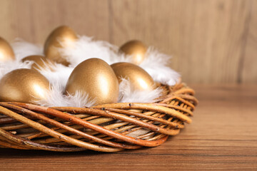 Golden eggs and feathers in nest on wooden table, closeup