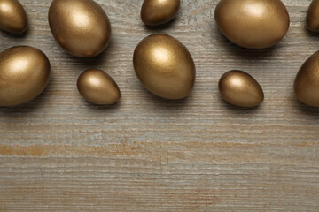 Fototapeta na wymiar Golden eggs on wooden table, flat lay. Space for text