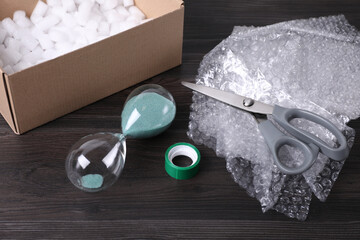 Sand hourglass, bubble wrap and packaging items on dark wooden table