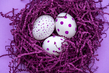 Colorful eggs in purple artificial bird's nest isolated on purple background. Easter concept.