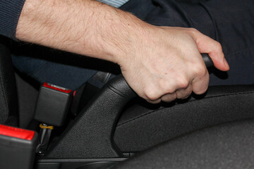 Close-up of a man's hand in a rubber glove pulling the handbrake lever in a car. The driver pulls on the handbrake in the car to activate the parking brake, the importance of the parking brake.