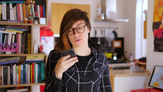 Beautiful woman recording message using voice on smartphone. Happy young woman recording audio on mobile phone ah home.