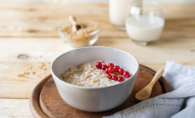 Healthy milky porridge from whole hulled grain oats with oat milk and red currant berries in bowl