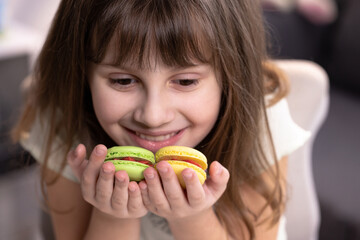 Smiling cute school kid girl holds four tasty cookies in her hands. Traditional French multicolored macaroon. Food concept