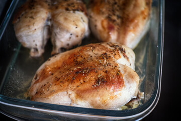 Roasted chicken breasts in a glass baking tray with spices on them