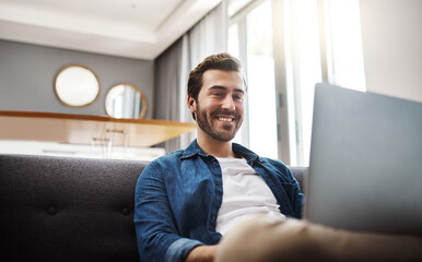 Theres always some cool stuff to watch on the internet. Shot of a handsome young man using his laptop while relaxing on a sofa at home.