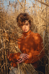 Portrait of beautiful young woman outdoor posing and holds a bouquet of reeds and looks straight at the camera
