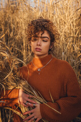 Portrait of beautiful young woman with curly hair while posing outdoor at sunset