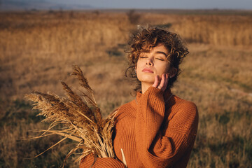 Portrait of a beautiful young female while enjoying the sun with closed eyes in the field of grass at sunset