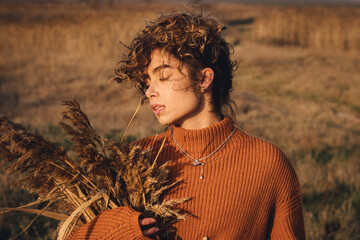 Portrait of a beautiful young woman while enjoying the sun with closed eyes in the field of grass at sunset