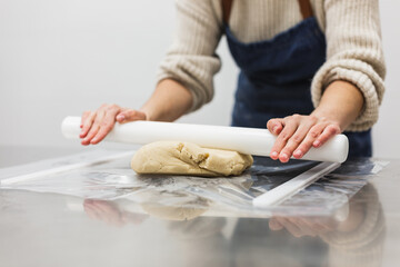 Close up view of a pastry chef kneading dough with a rolling pin at the kitchen table.