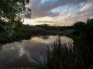 Lindo pôr do sol entre nuvens e árvores a beira de lagoa na zona rural do município de Esmeraldas, Minas Gerais.