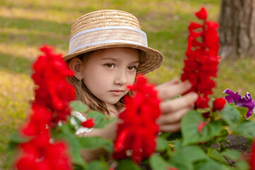 Cute brown-eyed preteen girl admiring blooming red flowers in summer park