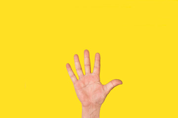 Mano de hombre con la palma abierta, gesticulando  el número cinco sobre un fondo amarillo liso y aislado. Vista de frente y de cerca. Copy space