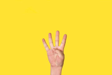 Mano de hombre con la palma abierta, gesticulando el número cuatro sobre un fondo amarillo liso y aislado. Vista de frente y de cerca. Copy space