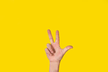 Mano de hombre con la palma abierta, gesticulando el número tres sobre un fondo amarillo liso y...