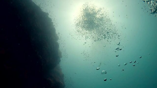 Underwater film 4 k - Thailand - under angeled shot of left flanked rock with rising air bubbles and shimmering sunlight above - very mesmerising