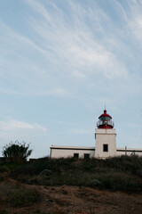 Fototapeta na wymiar Picture of lighthouse is located on green hills against blue sky. Edge of Europe. Clear sunny warm day