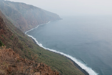 Fototapeta na wymiar Wide coastline of ocean connected with green hills in morning fog. Wild nature of edge of Europe