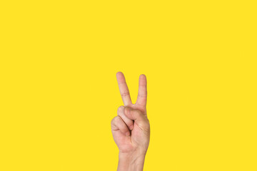 Mano de hombre con la palma abierta, gesticulando el número dos sobre un fondo amarillo liso y...