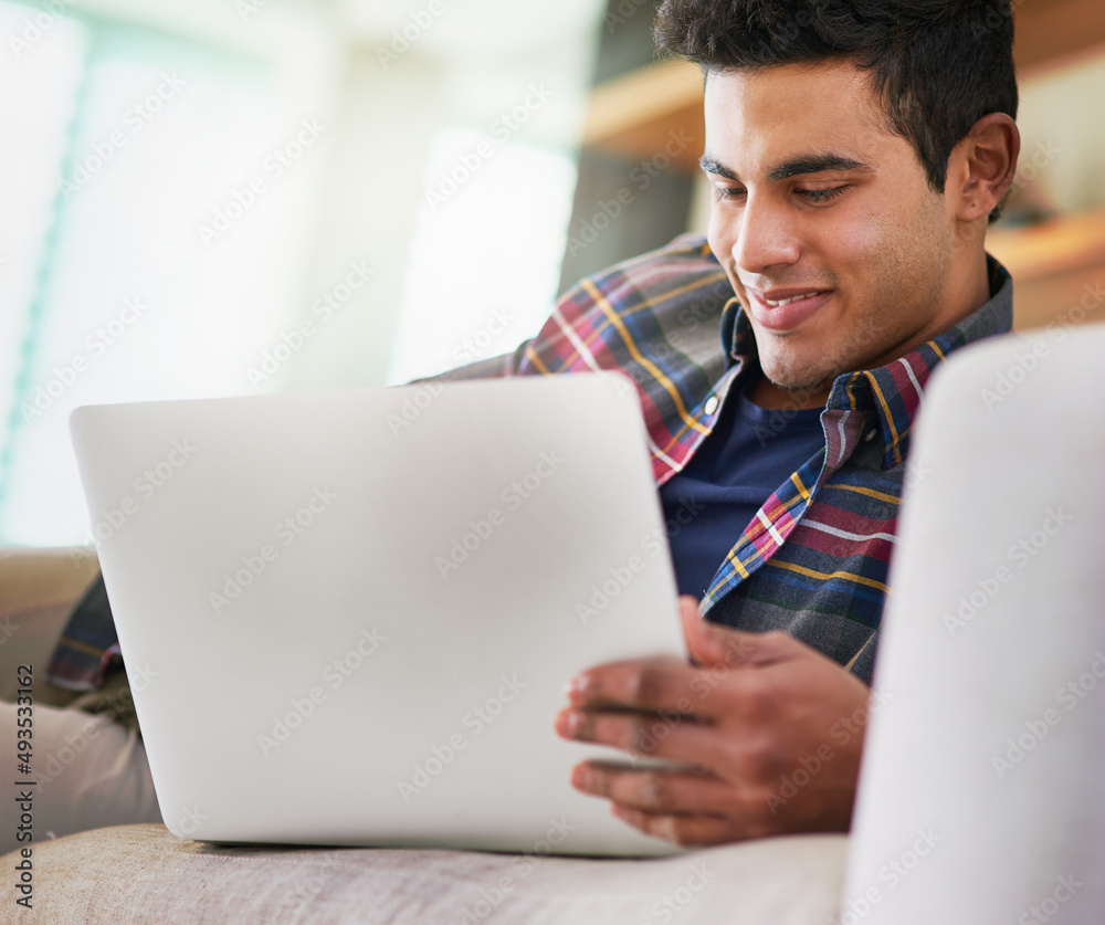 Poster spending a little time online. shot of a handsome young man using his laptop while relaxing on the s