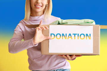 Woman holding donation box with clothes against Ukrainian flag. Humanitarian assistance for...
