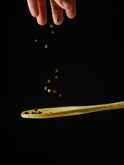 Wooden spoon and black peppercorns in frozen flight. Isolated on black background. Close-up. There are no people in the photo. Seasonings, spices. Advertising, banner.
