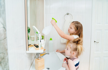 cute little girls washes sink and the bathroom mirror with a special cleaner.