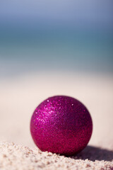 Pink Christmas glitter ball on the sand. Selective focus