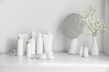 Different cosmetic products, mirror and gypsophila flowers on table