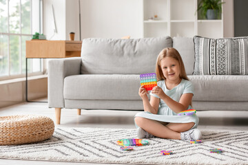 Little girl sitting on floor and holding pop it fidget toy in room - obrazy, fototapety, plakaty